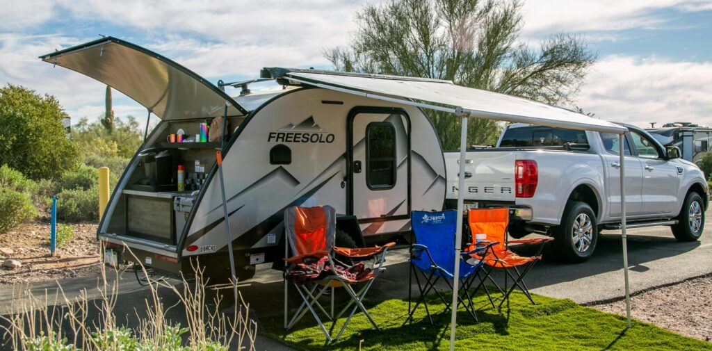 A scenic campsite in Apache Junction, AZ showcasing a Freesolo motorhome with camping chairs and pickup truck.
