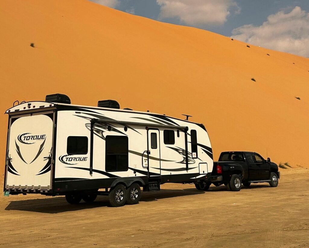 Explore the vast Abu Dhabi desert landscape with a travel RV and truck under a clear blue sky.