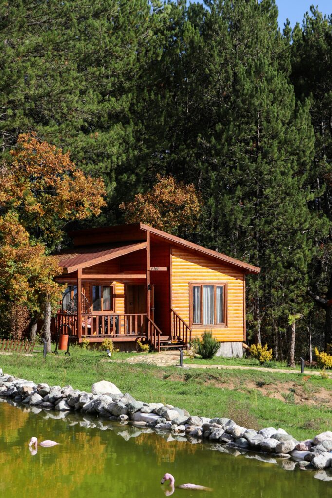 Charming wooden cabin nestled by a pond in a serene forest setting, ideal for retreats and nature escapes.