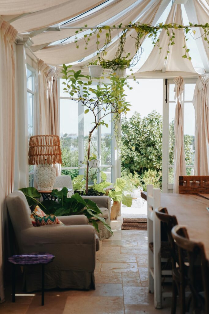 Bright conservatory room filled with natural light, plants, and comfortable seating.