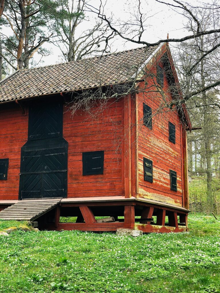 Red wooden barn surrounded by lush green forest in Jönköping County, Sweden.