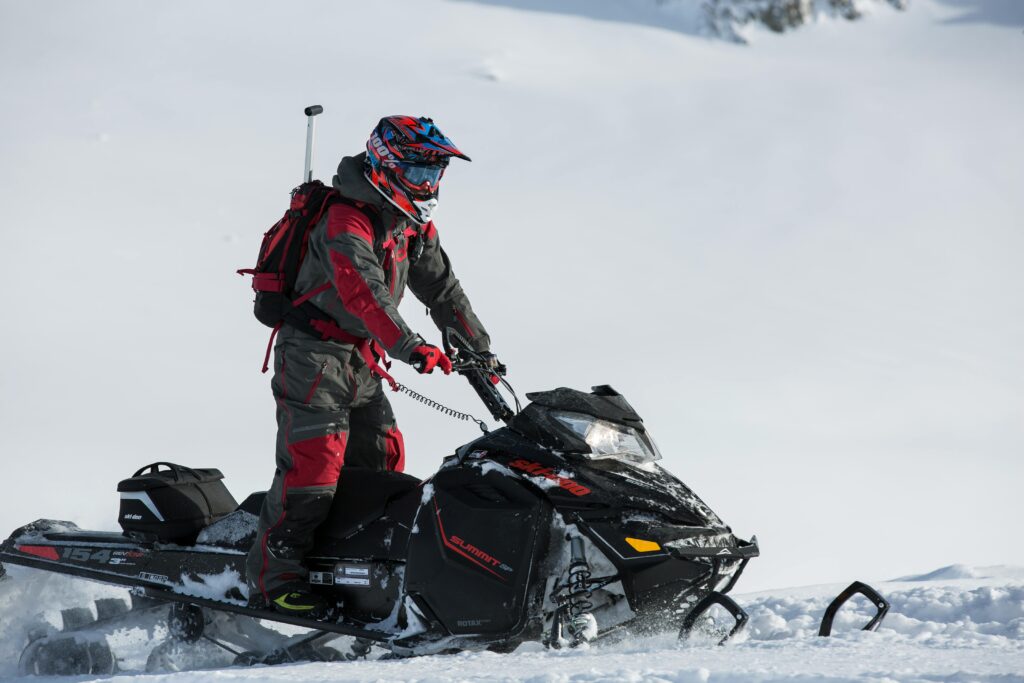 Snowmobiler navigating snowy terrain wearing protective gear and helmet.