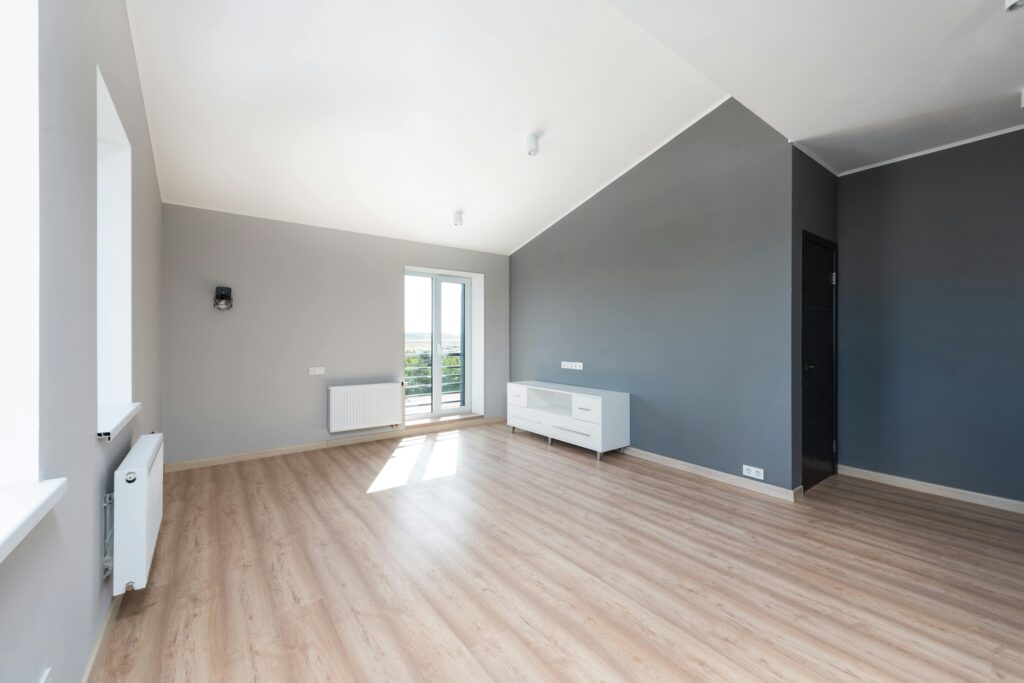 Wide-angle shot of a modern unfurnished apartment with wooden flooring and large windows.