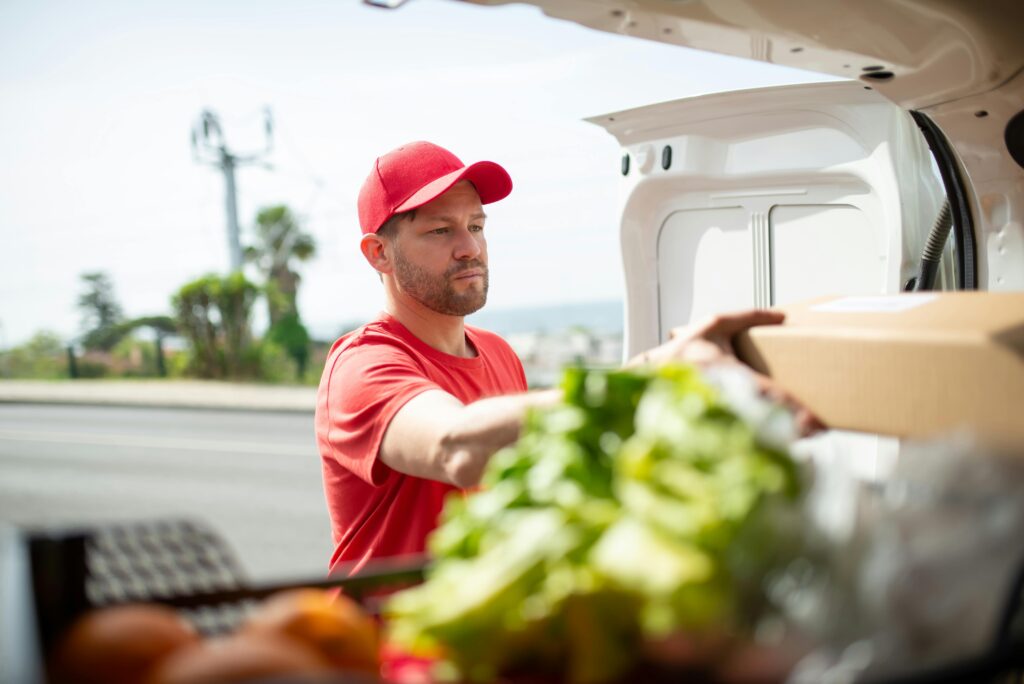 A male delivery driver in a red uniform handling a parcel from a vehicle outdoors in Portugal.