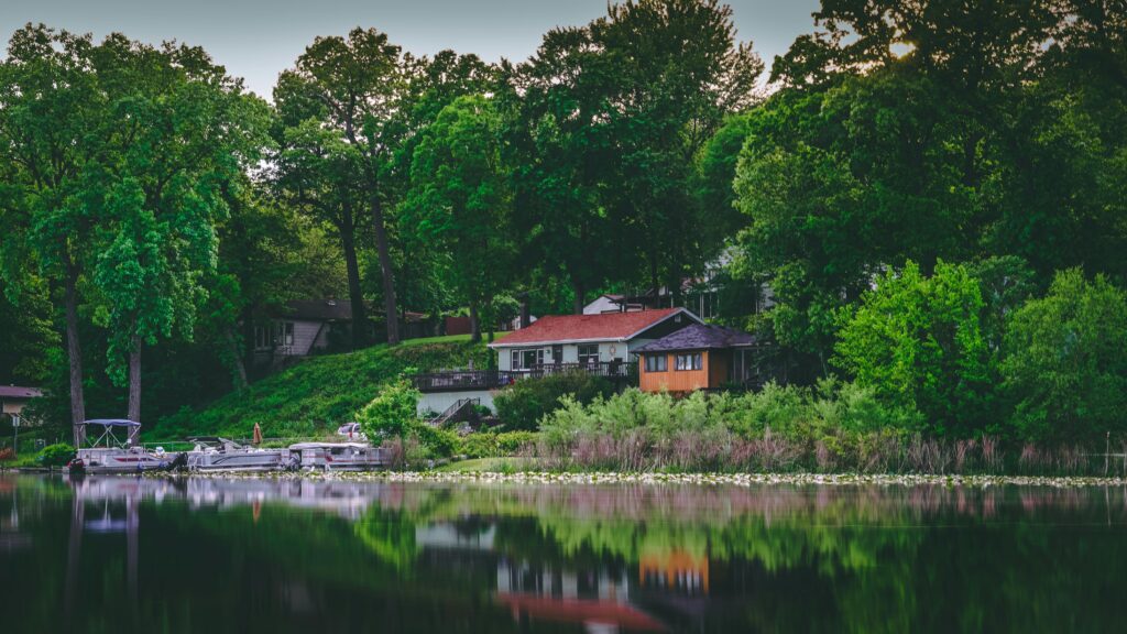 Serene lakefront house surrounded by lush green trees and calm waters, perfect for relaxation.