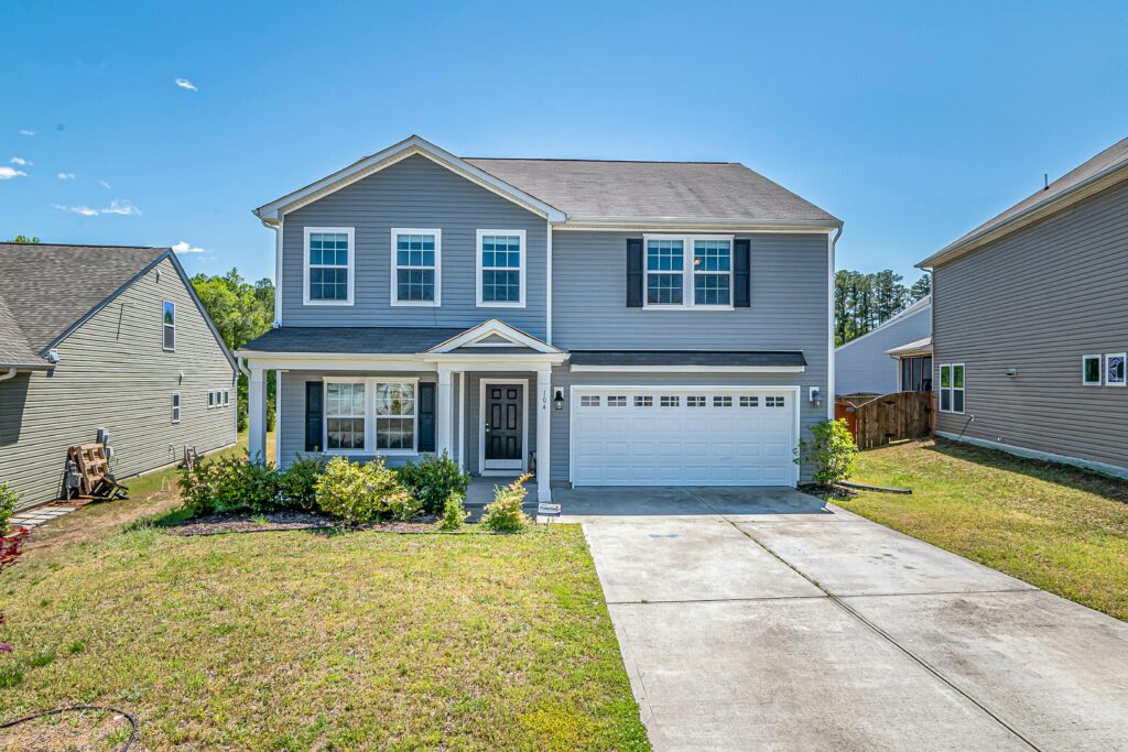 A modern two-story house with a large driveway and landscaped front yard under clear blue skies.